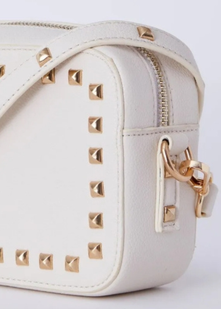 a rectangular white vegan leather handbag adorned with gold studs. The handbag exudes a chic and sophisticated vibe, perfect for elevating any outfit. With its stylish gold stud detailing, this vegan leather bag is a must-have accessory for those seeking a blend of elegance and modern edge. Ideal for both casual and formal occasions