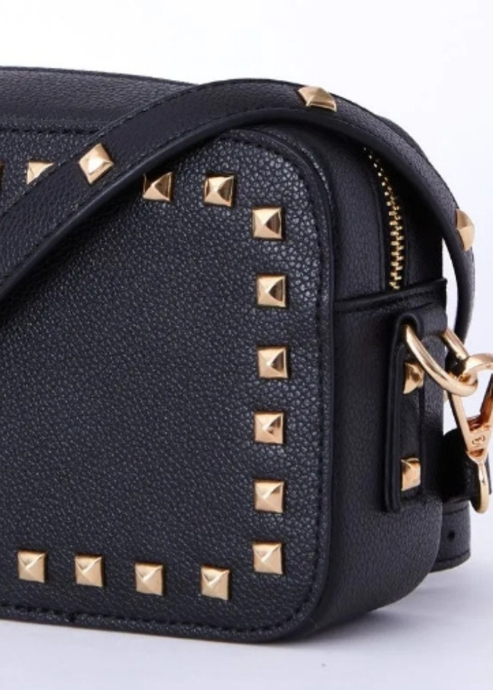 a rectangular black vegan leather handbag adorned with gold studs. The handbag exudes a chic and sophisticated vibe, perfect for elevating any outfit. With its stylish gold stud detailing, this vegan leather bag is a must-have accessory for those seeking a blend of elegance and modern edge. Ideal for both casual and formal occasions