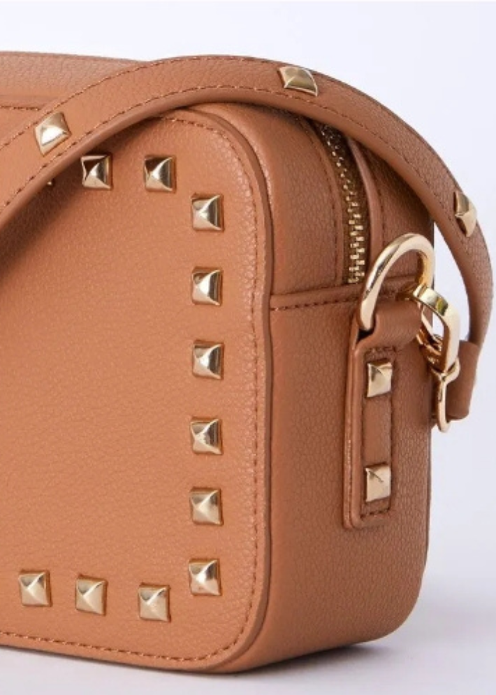 a rectangular tan vegan leather handbag adorned with gold studs. The handbag exudes a chic and sophisticated vibe, perfect for elevating any outfit. With its stylish gold stud detailing, this vegan leather bag is a must-have accessory for those seeking a blend of elegance and modern edge. Ideal for both casual and formal occasions