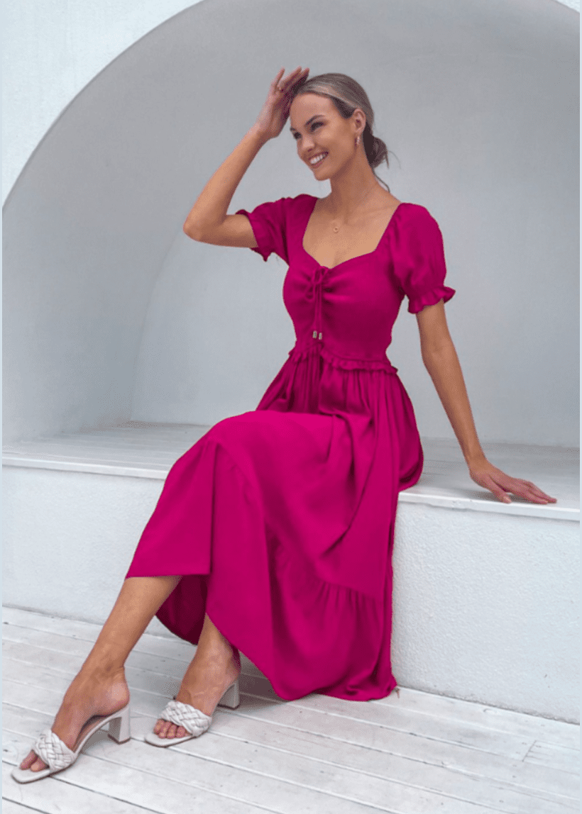 Vibrant fuchsia midi dress with puff sleeves and a subtle sweetheart neckline featuring a front tie detail. The dress has a cinched waist and a flowing skirt that reaches mid-calf, creating an elegant silhouette. Dress by Mylk the Label. Available in sizes 8-16