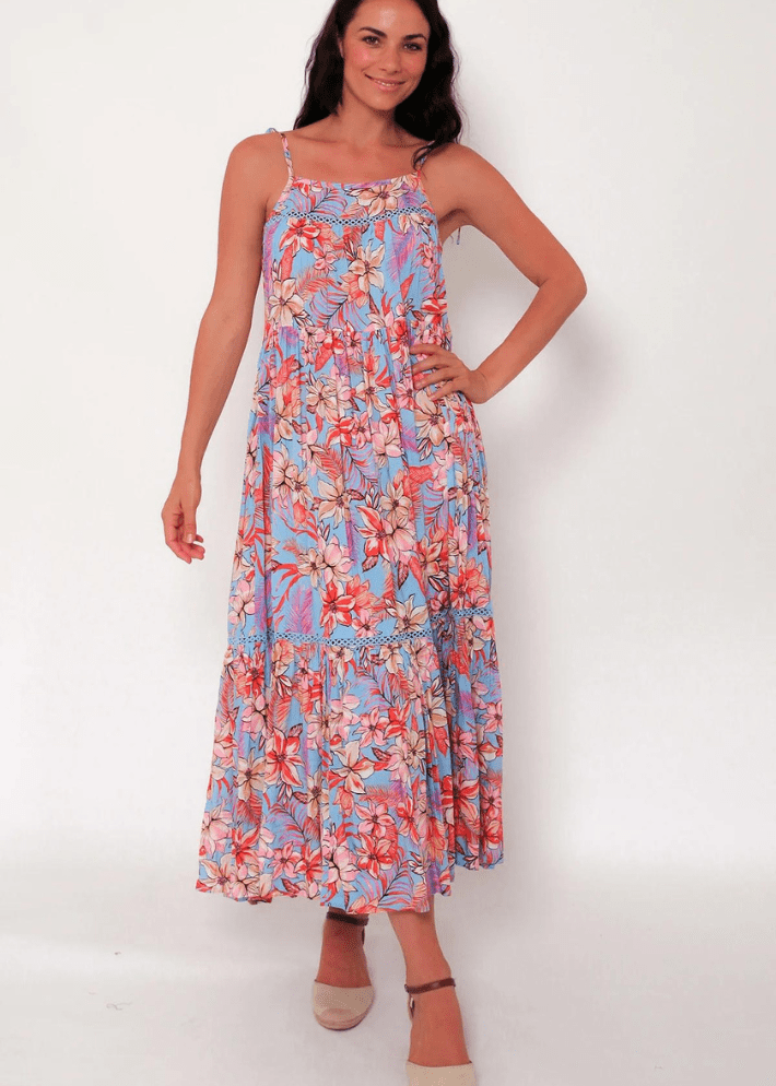 Women's sleeveless maxi dress with pink, orange, and white floral design on a light blue background. It has tie spaghetti straps and a tiered skirt.