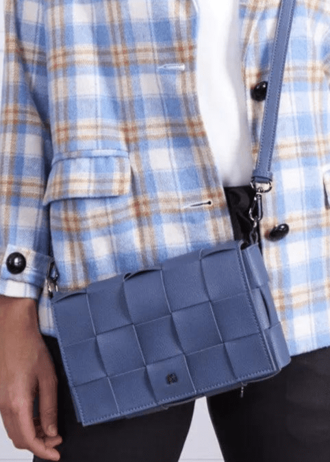 A woman wearing a blue crossbody handbag made of vegan leather, featuring a woven texture and adjustable straps AG47