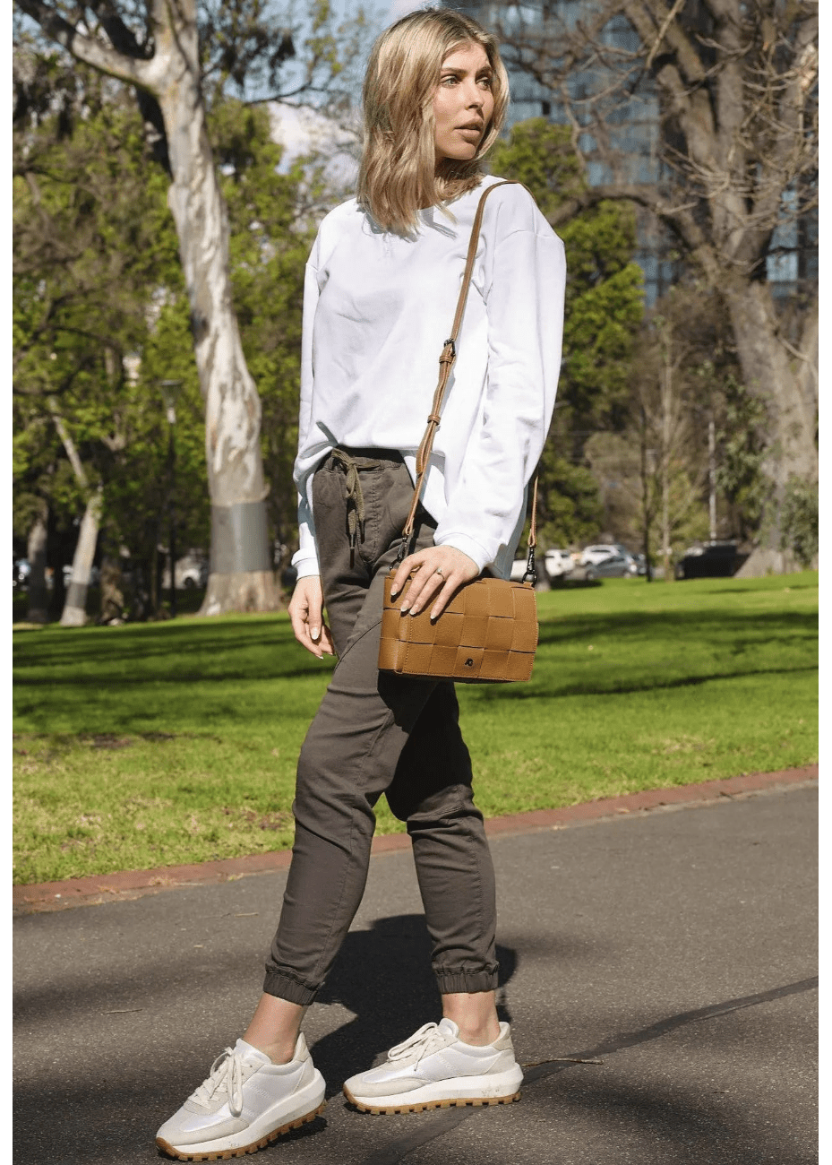 A woman wearing a tan crossbody handbag made of vegan leather, featuring a woven texture and adjustable straps