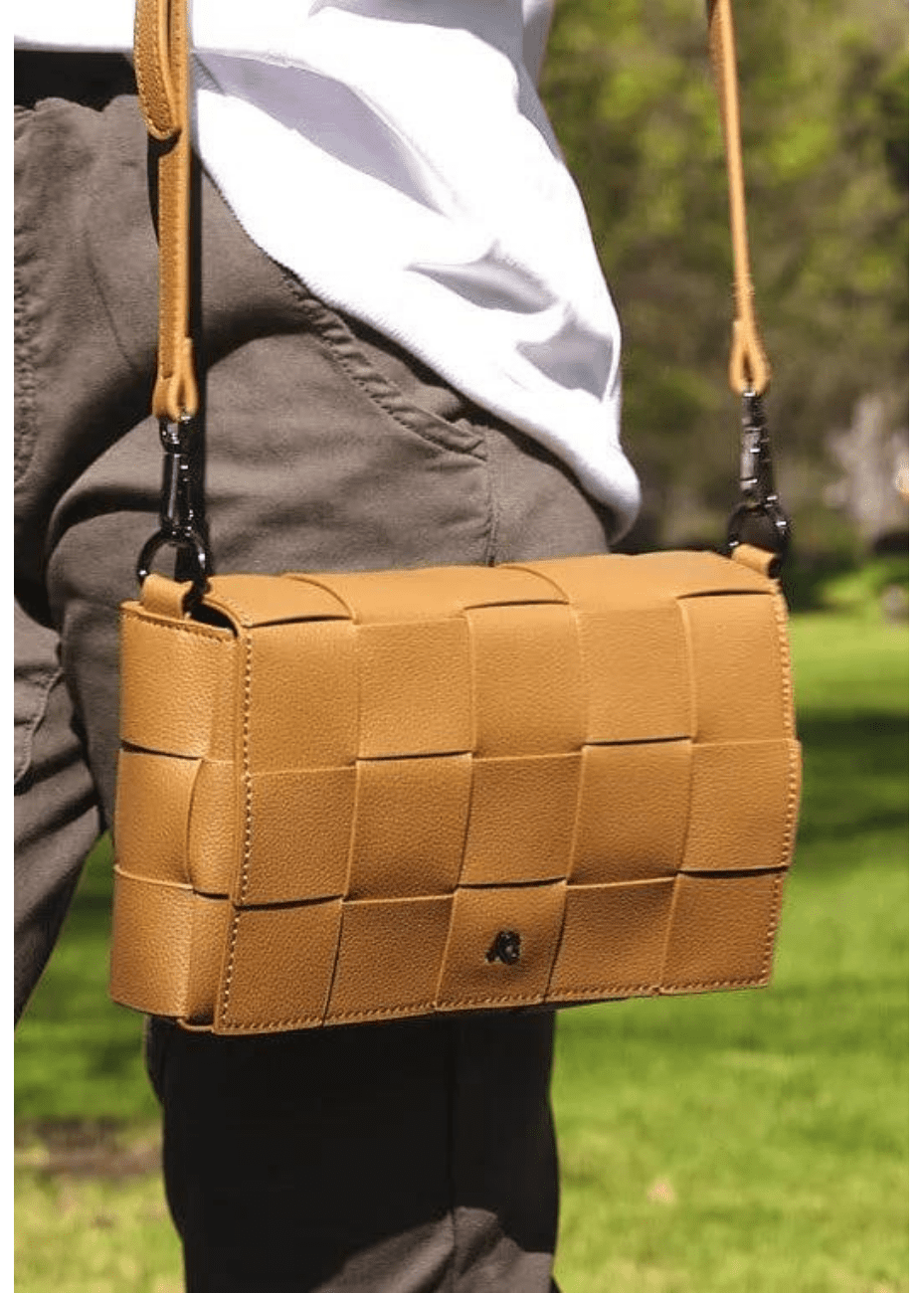 A woman wearing a tan crossbody handbag made of vegan leather, featuring a woven texture and adjustable straps