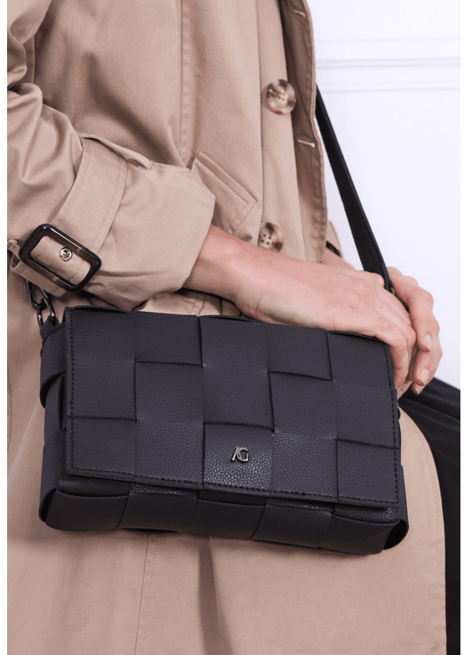 A woman wearing a black crossbody handbag made of vegan leather, featuring a woven texture and adjustable straps