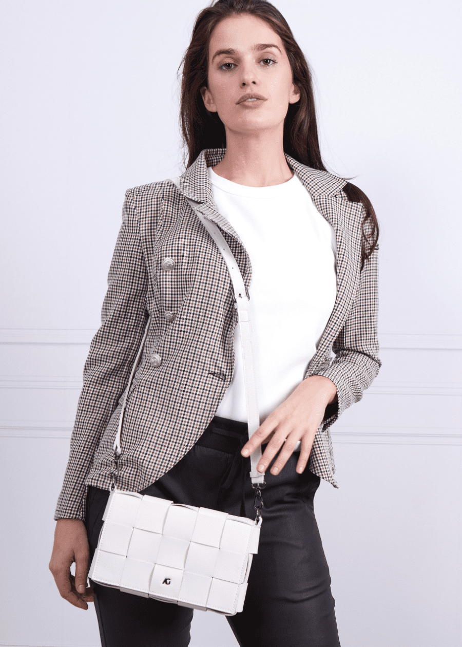 A woman wearing a white crossbody handbag made of vegan leather, featuring a woven texture and adjustable straps