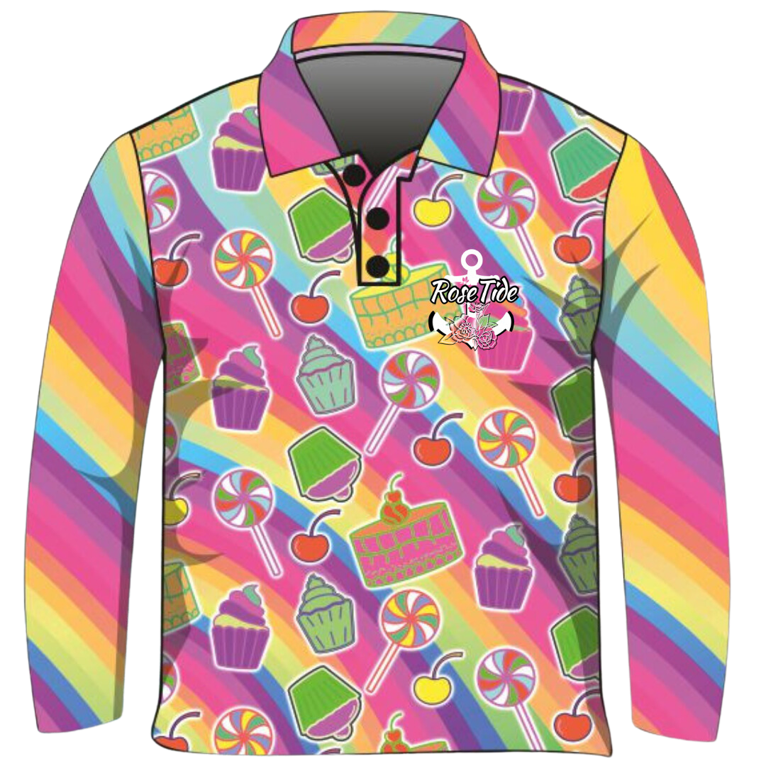 A long sleeve children's fishing shirt with a colourful, playful pattern featuring various sweets, including cupcakes, lollipops, cherries, and cakes. The background is a rainbow of diagonal stripes in vibrant hues. The "Rose Tide" logo with an anchor and floral design is displayed on the chest.