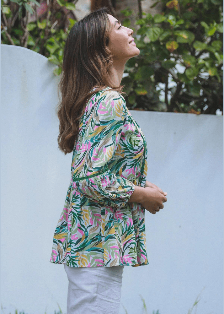 This vibrant top blooms with style, featuring a lush garden of tropical leaves and exotic flowers, a symphony of pink, green, and yellow hues that dance across the fabric. The playful peplum silhouette flares gently at the waist, creating a breezy and flattering shape that sings of carefree summer days. With its long sleeves gathered at the wrists, it strikes a perfect balance between comfort and chic, making it a versatile choice for both a casual brunch or a stroll through the city's botanical gardens.