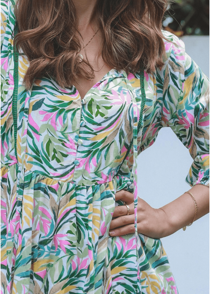 Ava top from Ava & Mia – a stunning tropical leaf print blouse that comes in sizes 8 to 16. The lace-trimmed V-neckline is accentuated by four functional buttons that add a touch of elegance. This stylish top is tailored from high-quality rayon material to ensure a soft and comfortable fit. The vivid greens, pinks, and yellows pattern make it perfect for any summer wardrobe. With an empire waist and elastic-cuffed three-quarter sleeves, this top is both fashionable and practical.