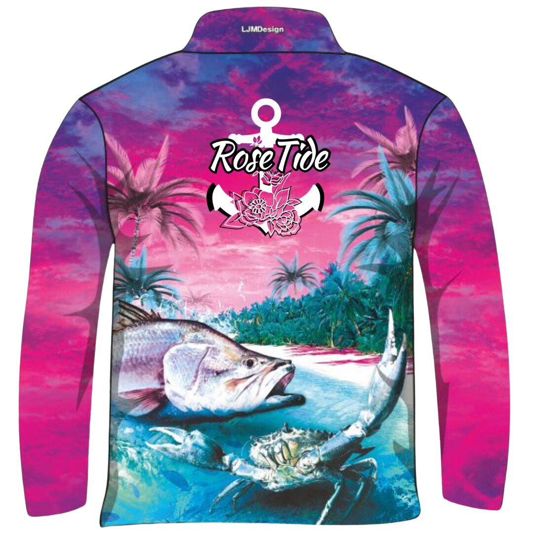 A long sleeve women's fishing shirt with a vibrant, tropical design featuring palm trees, a barra, and a crab in a colourful sunset beach scene. The shirt has the logo "Rose Tide" with an anchor and floral design on the back.