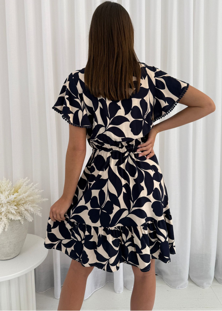 woman in the Celine Mini Dress, a summer boho-style navy blue and cream floral dress with a V-neckline, flutter sleeves, and a drawstring waist.