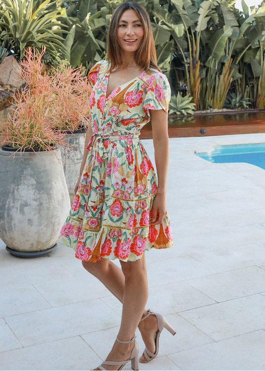 Elara Mini Dress with tropical floral print in pink, red, and orange hues on a yellow base, perfect for boho summer style. showcasing flutter sleeves and a lightweight, breezy design