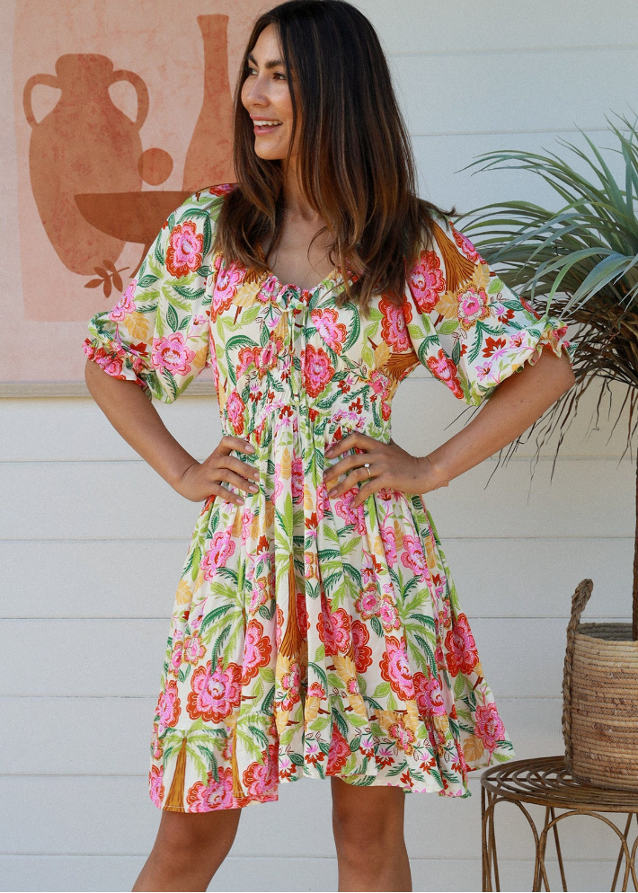 Summer Mini Dress with tropical palm and floral print in vivid pink, green, and yellow tones. Adjustable drawstring neckline and feminine puff sleeve details