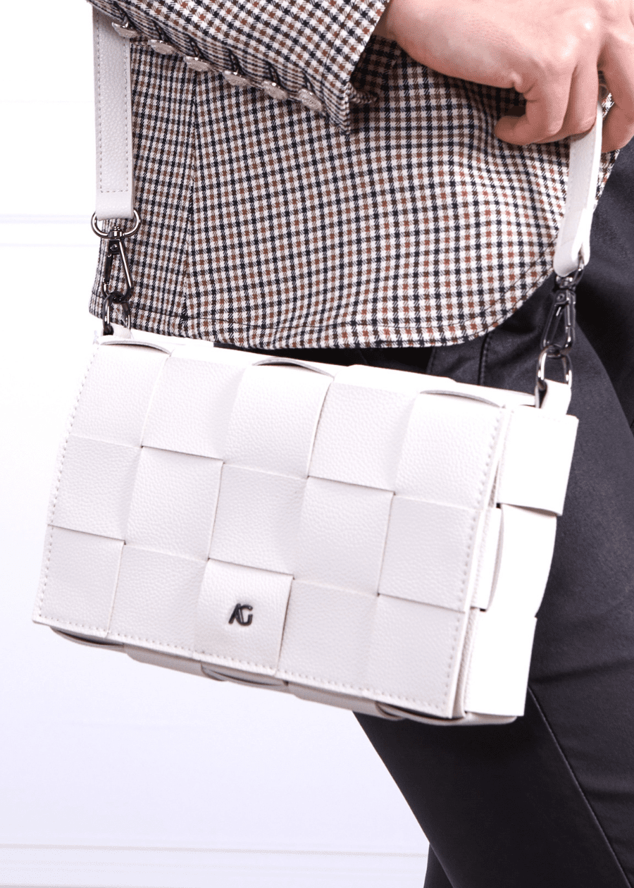 A woman wearing a white crossbody handbag made of vegan leather, featuring a woven texture and adjustable straps