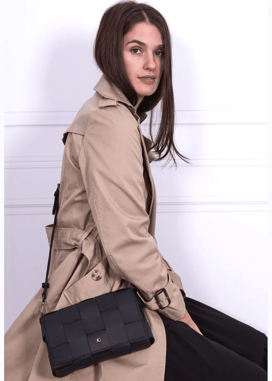 A woman wearing a black crossbody handbag made of vegan leather, featuring a woven texture and adjustable straps