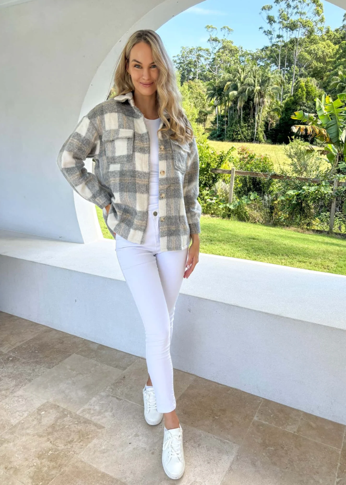 A woman wearing a relaxed-fit plaid jacket in shades of grey and white, featuring button details and front pockets. She paired the jacket with a white top and white high-waisted pants, creating a cozy and stylish outdoor look.