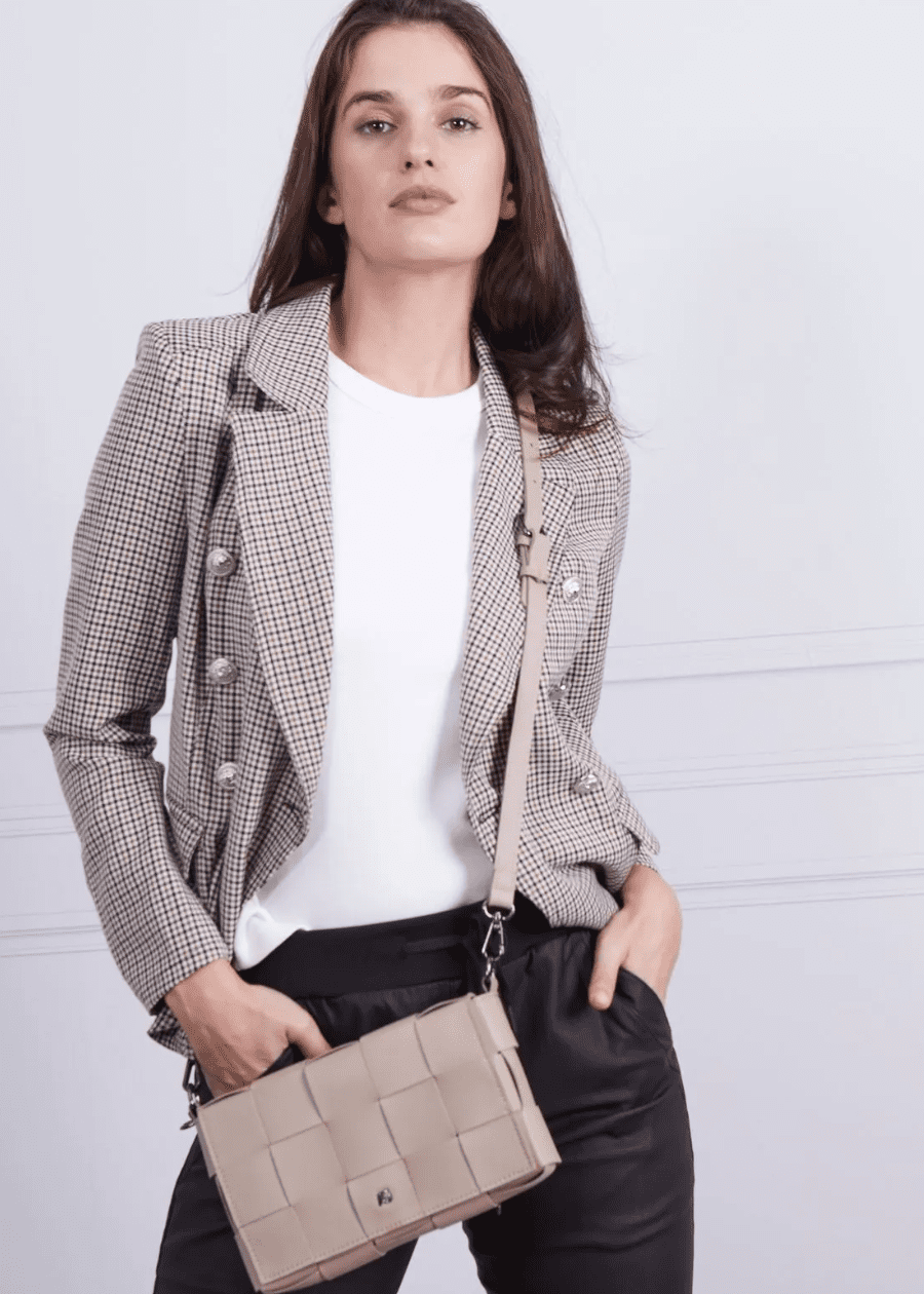 A woman wearing a beige crossbody handbag made of vegan leather, featuring a woven texture and adjustable straps