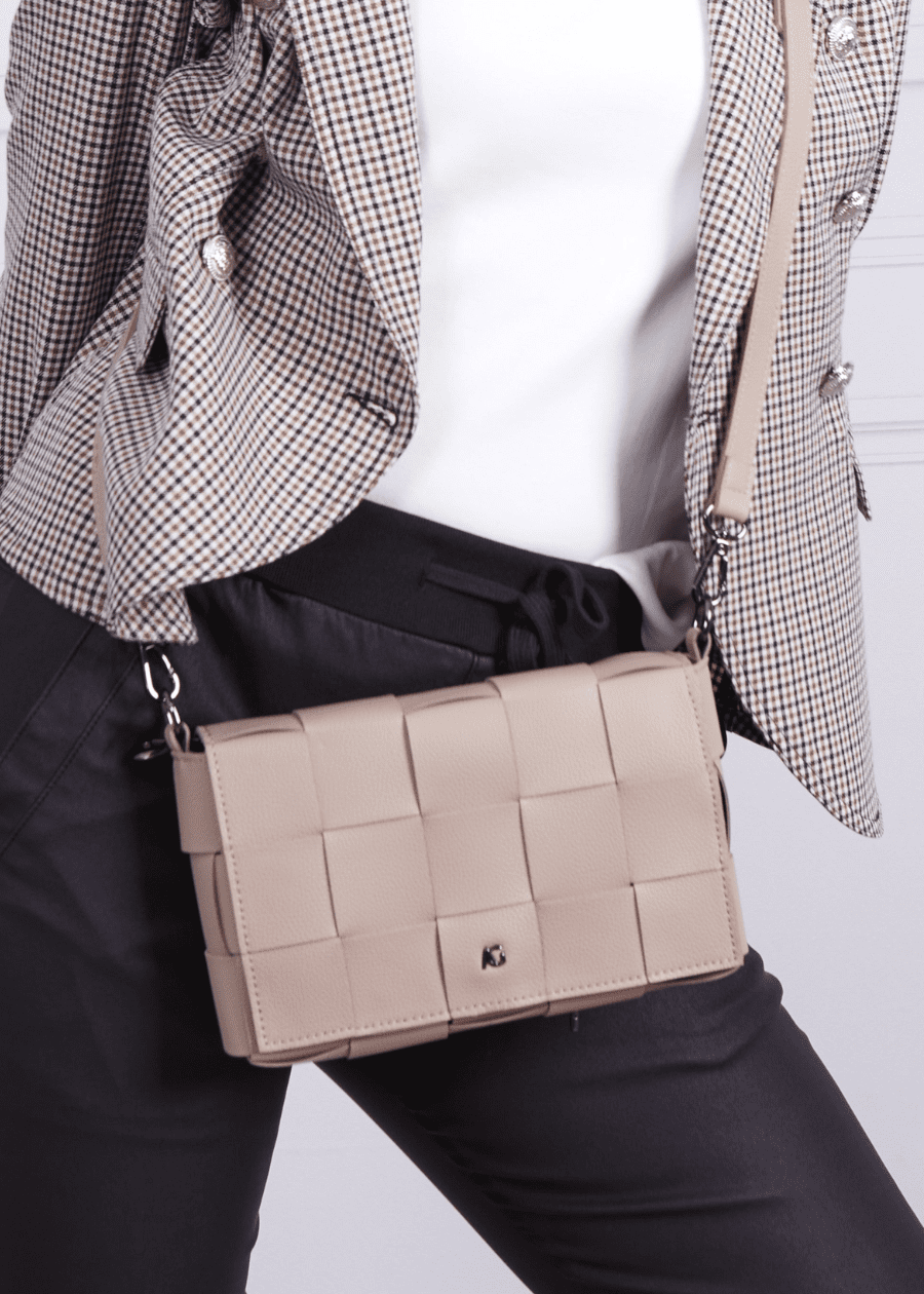 A woman wearing a beige crossbody handbag made of vegan leather, featuring a woven texture and adjustable straps