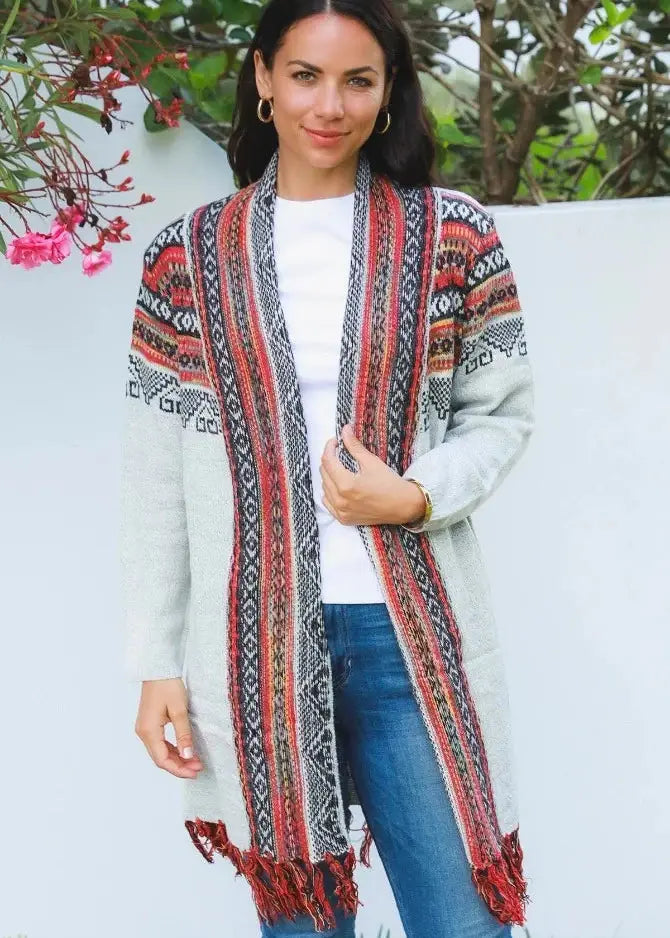 A woman wearing a white open above the knee length knit cardigan with detailed red and black tribal patterns.