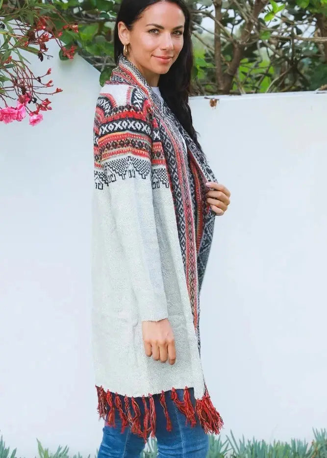 A woman wearing a white open above the knee length knit cardigan with detailed red and black tribal patterns